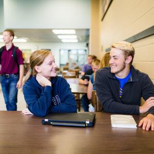 Students seated at a table at M State smile at each other